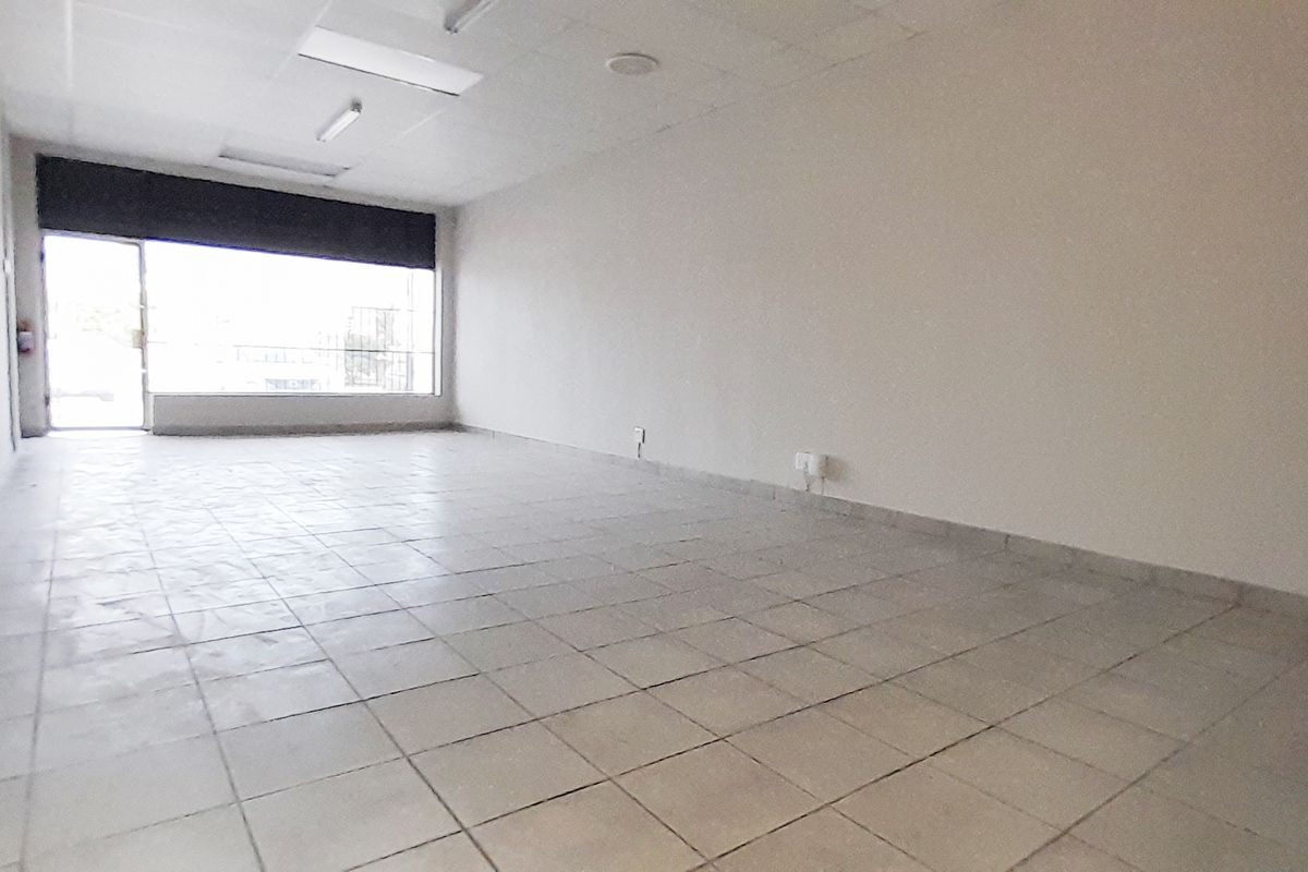 An empty, open-plan retail space featuring tiled flooring, a suspended ceiling with integrated lighting, and a large glass storefront window.