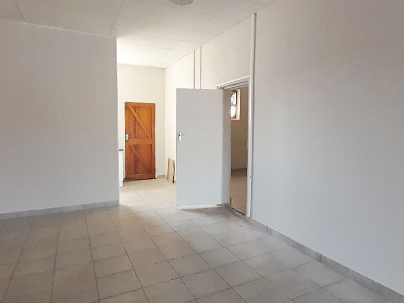 An empty, utilitarian retail space featuring tiled flooring, a drop ceiling, and multiple internal access doors.