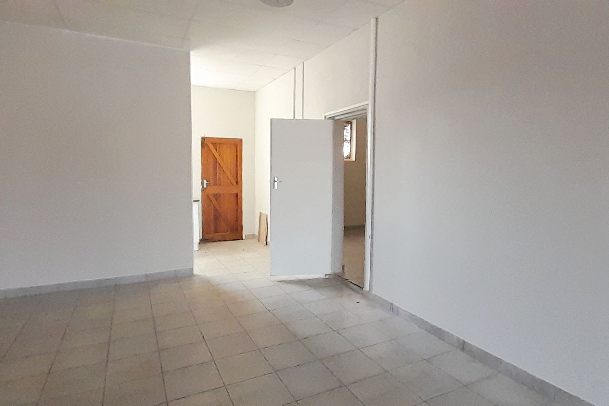 An empty, utilitarian retail space featuring tiled flooring, a drop ceiling, and multiple internal access doors.