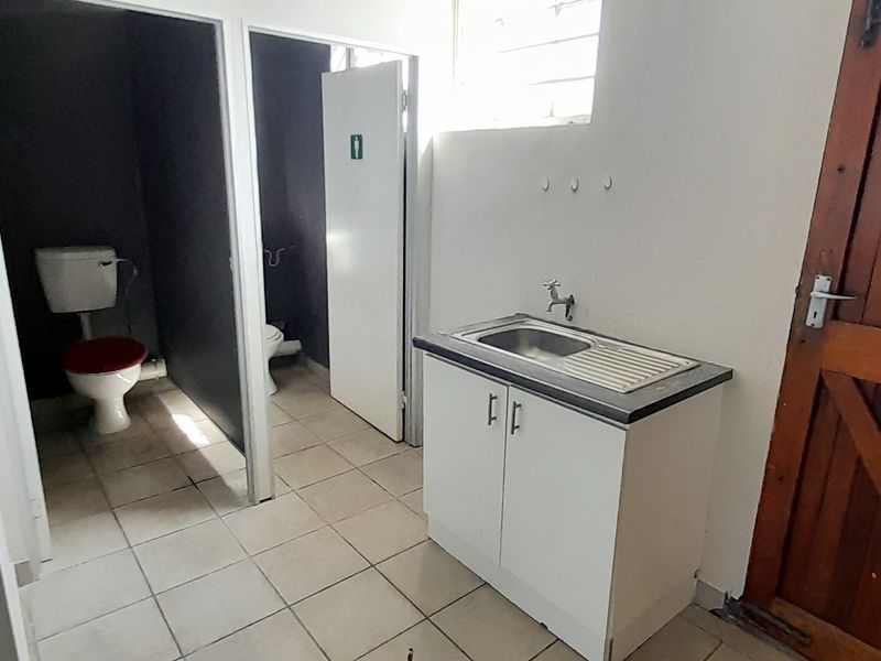 A functional bathroom area featuring a vanity sink, tiled flooring, and separate toilet cubicles with basic finishes.