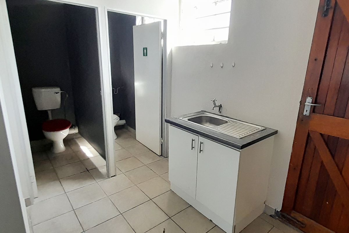 A functional bathroom area featuring a vanity sink, tiled flooring, and separate toilet cubicles with basic finishes.