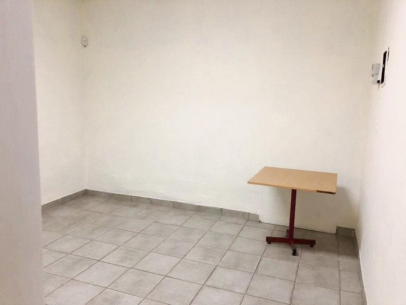 A simple, empty utility space featuring neutral ceramic floor tiles and plain white walls, suitable for storage or a small office area.