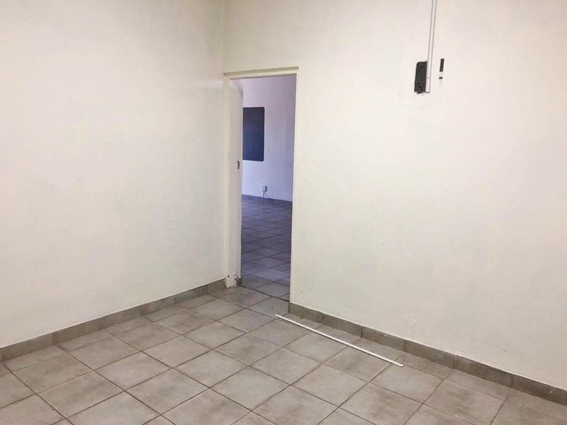 An empty, neutral-toned room featuring tiled flooring and visible electrical conduit, providing a blank canvas for retail or office use.