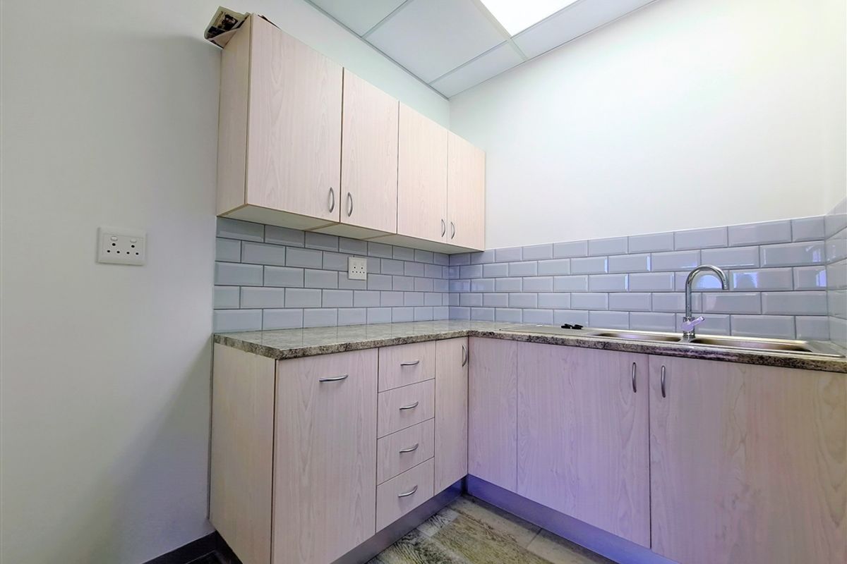 A functional office kitchenette featuring light wood cabinetry, granite-look countertops, a stainless steel sink, and subway tile backsplash.