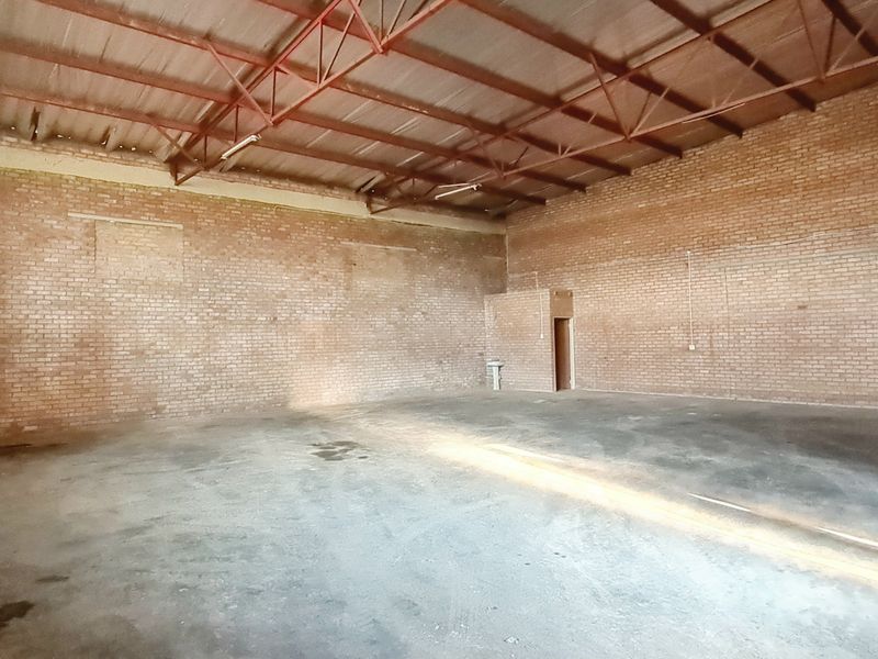 Spacious industrial warehouse unit featuring exposed brick walls, high-clearance steel roof trusses, and durable concrete flooring, suitable for various commercial or storage applications.