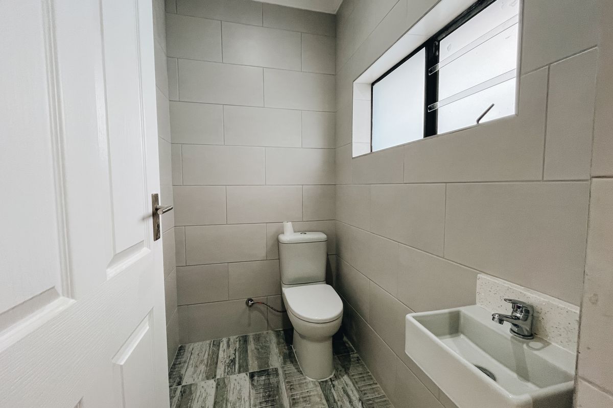 A modern, compact guest bathroom featuring neutral wall tiling, wood-look floor tiles, a wall-mounted basin, and a standard toilet.