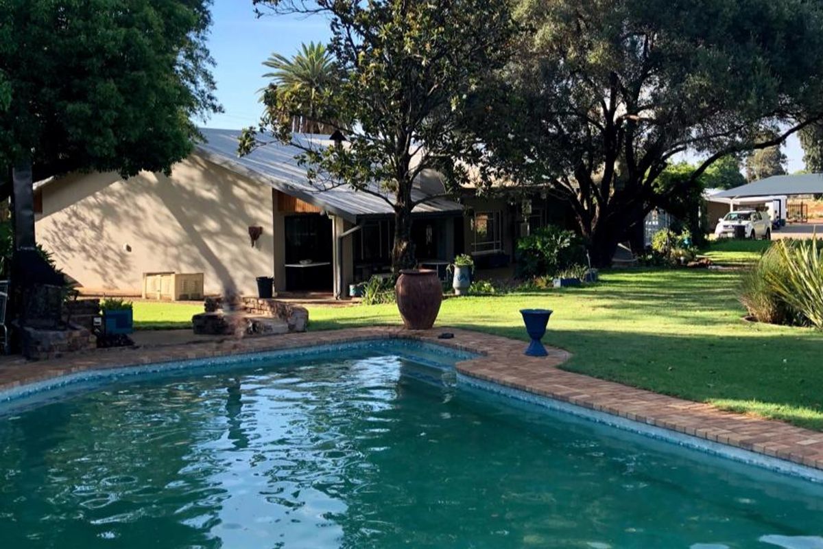 A well-maintained swimming pool area featuring brick coping, expansive green lawn, and mature trees, set against the rear elevation of the farm property.