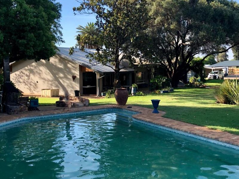 A well-maintained swimming pool area featuring brick coping, expansive green lawn, and mature trees, set against the rear elevation of the farm property.