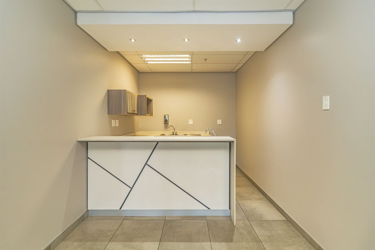 A functional kitchenette area featuring a modern built-in counter, stainless steel sink, overhead cabinetry, and tiled flooring within an industrial office space.