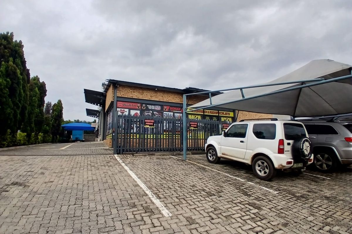 Industrial property exterior featuring a brick facade, secure metal fencing, and a covered parking area with shade cloth structure.