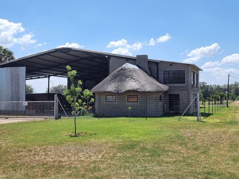 Front view of a small holding property featuring a combination of a traditional thatched roof structure and a large industrial-style corrugated metal shed.