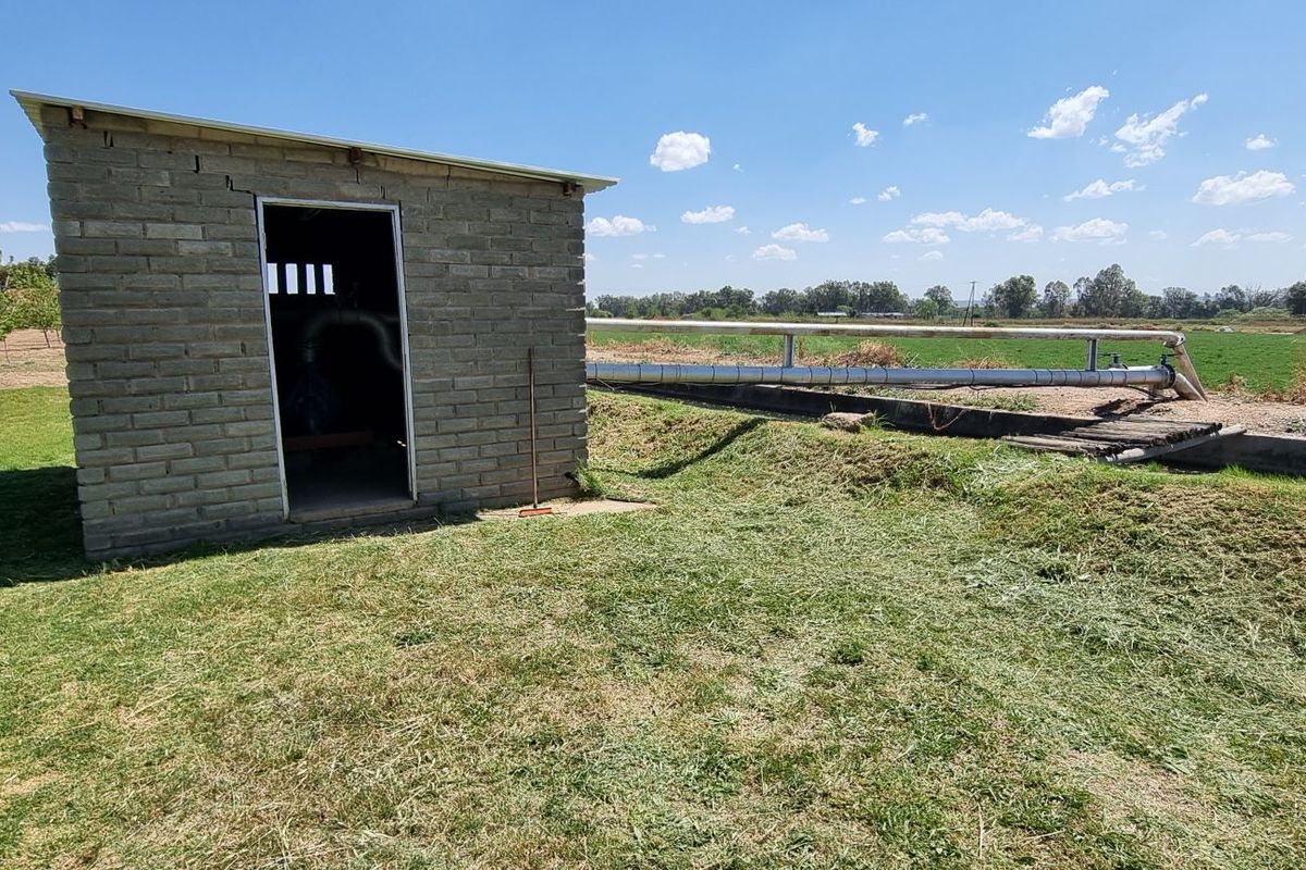 A functional brick pump house structure located on the small holding, featuring external irrigation piping and agricultural land surroundings.