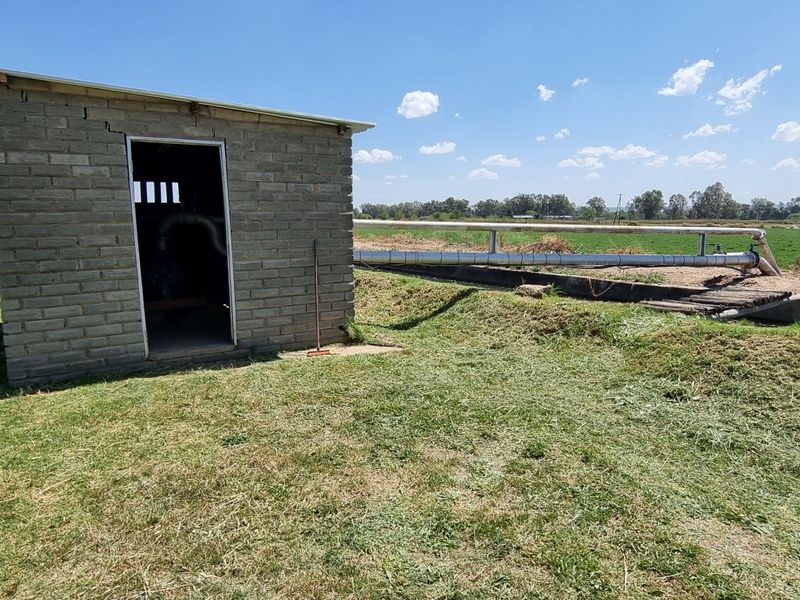 A functional brick pump house structure located on the small holding, featuring external irrigation piping and agricultural land surroundings.