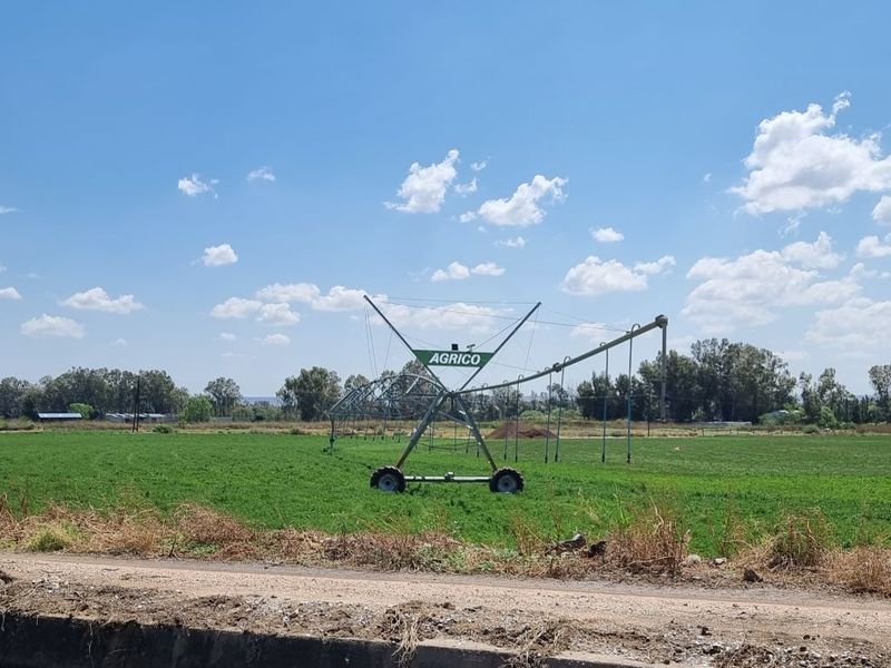 Expansive agricultural land featuring a center pivot irrigation system and a concrete irrigation canal, suitable for farming operations.
