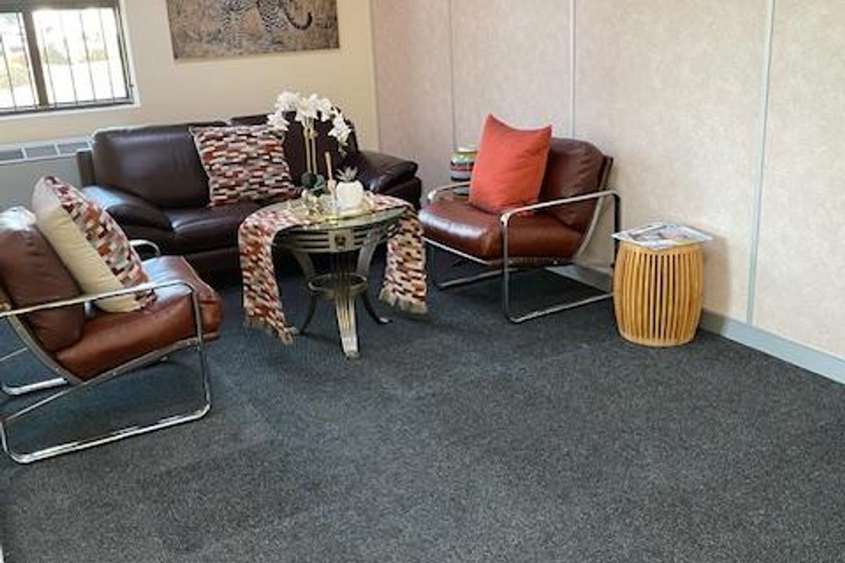 A functional office waiting area featuring modular wall panels, grey carpet tiles, and a window with security bars.