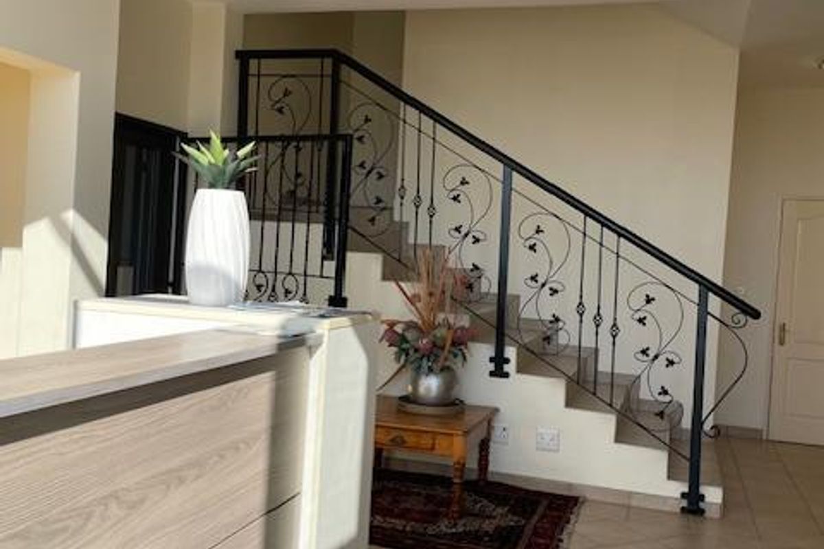 A bright office reception area featuring a staircase with decorative wrought iron railings and tiled flooring.