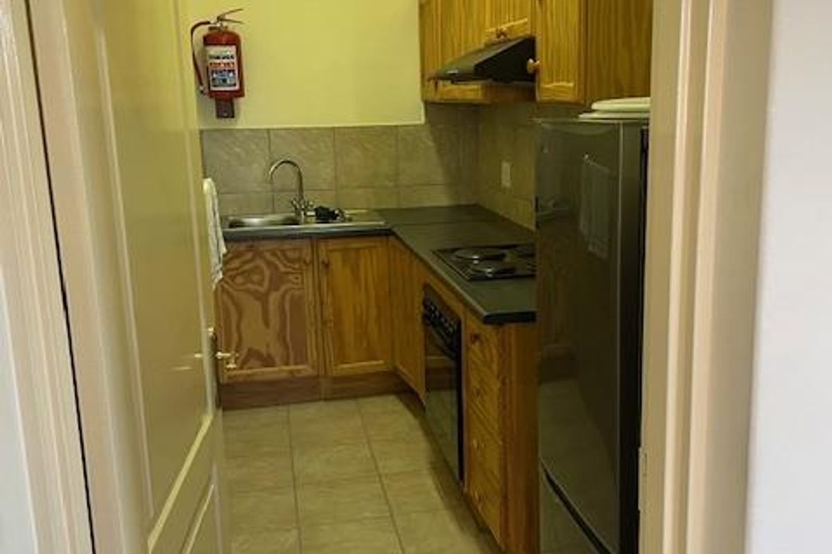 A compact office kitchenette featuring wooden cabinetry, a built-in hob, oven, extractor fan, and a stainless steel sink with tiled splashbacks.