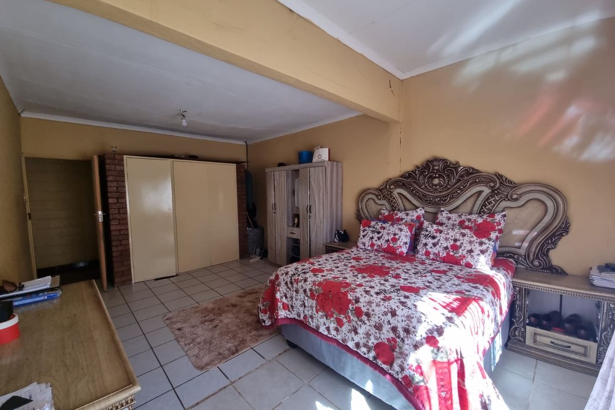 Spacious bedroom featuring tiled flooring, built-in cupboards, and an exposed brick accent wall, requiring some cosmetic updates to the wall and ceiling finishes.