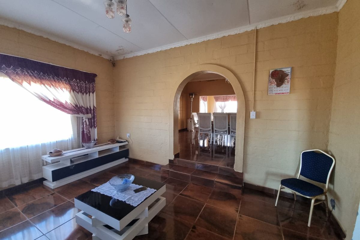 Living room featuring tiled floors, exposed blockwork walls, and an arched doorway leading to the dining area, with visible ceiling water damage.