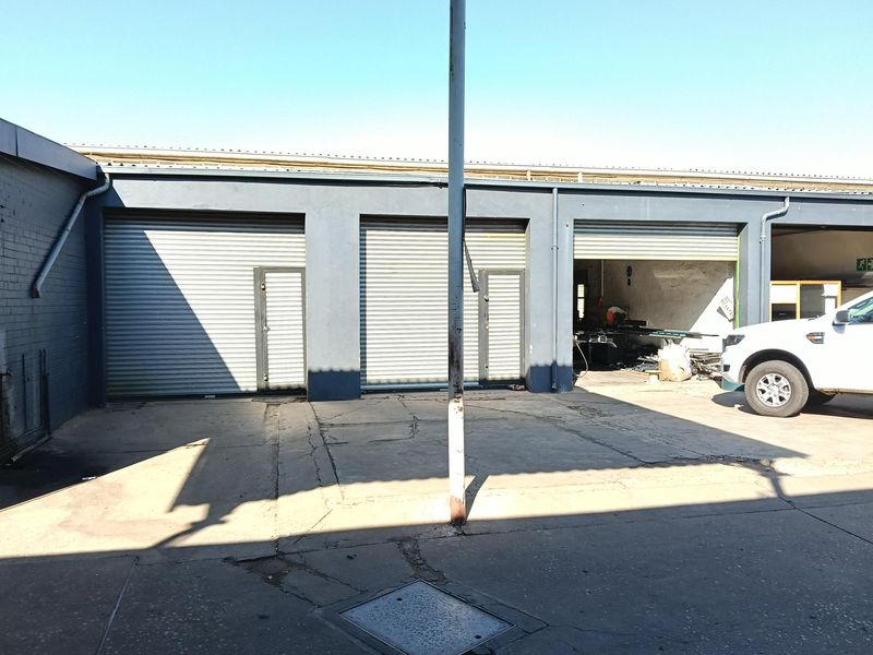 Industrial property exterior featuring multiple roller shutter doors and a concrete driveway with visible surface wear.