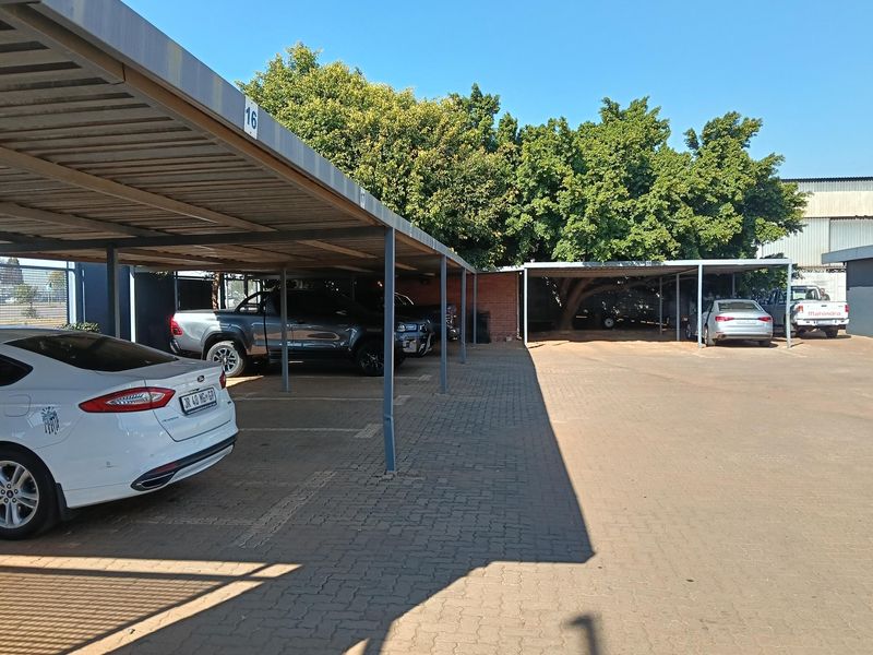 Industrial property featuring a paved parking area with multiple covered steel carport bays and mature trees.