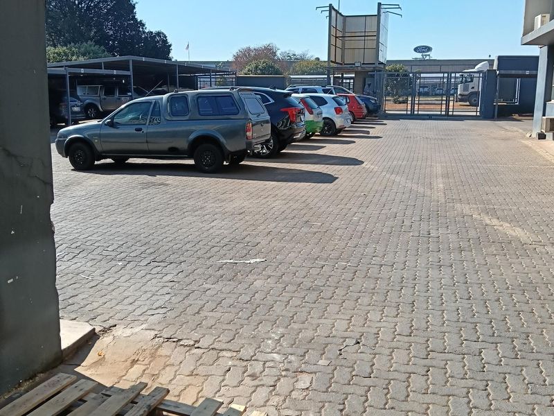Industrial property exterior featuring a paved parking area with covered bays and secure gated access.