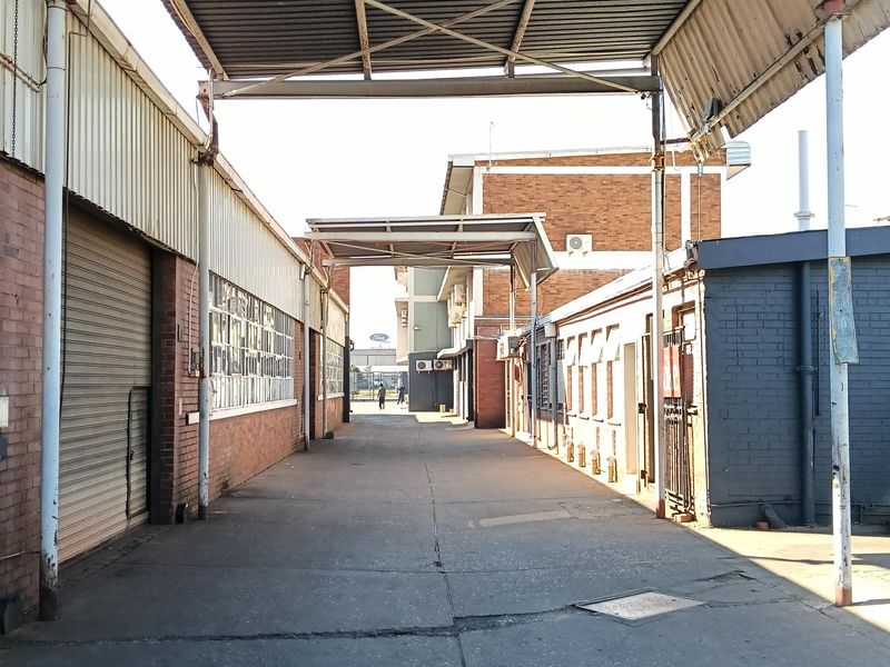 Industrial exterior corridor featuring a covered loading area, concrete driveway, and brick building facades with roller shutter access.