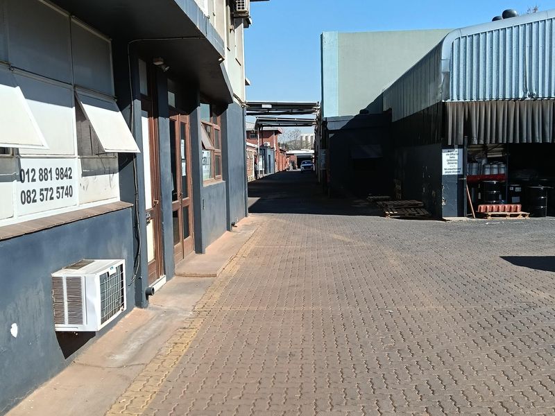 Exterior view of an industrial property featuring a paved driveway, metal cladding, and external air conditioning units along the building facade.