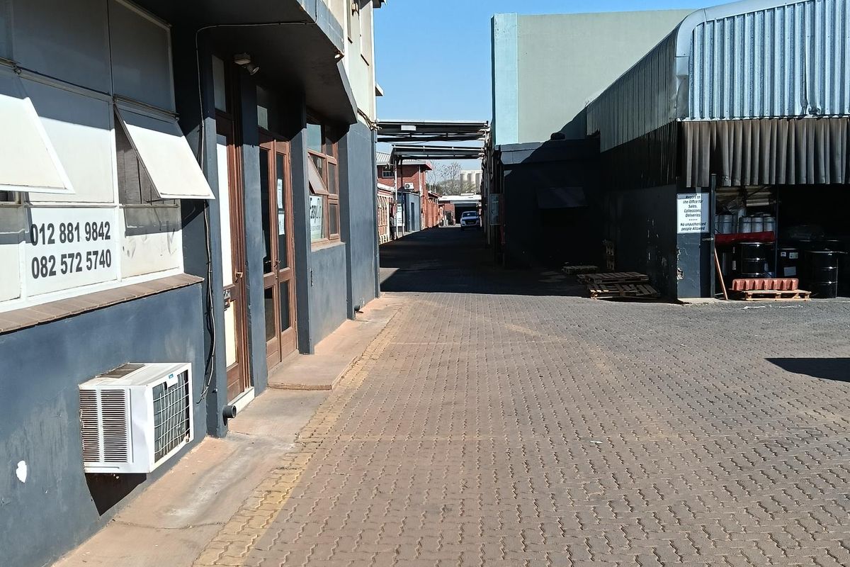 Exterior view of an industrial property featuring a paved driveway, metal cladding, and external air conditioning units along the building facade.
