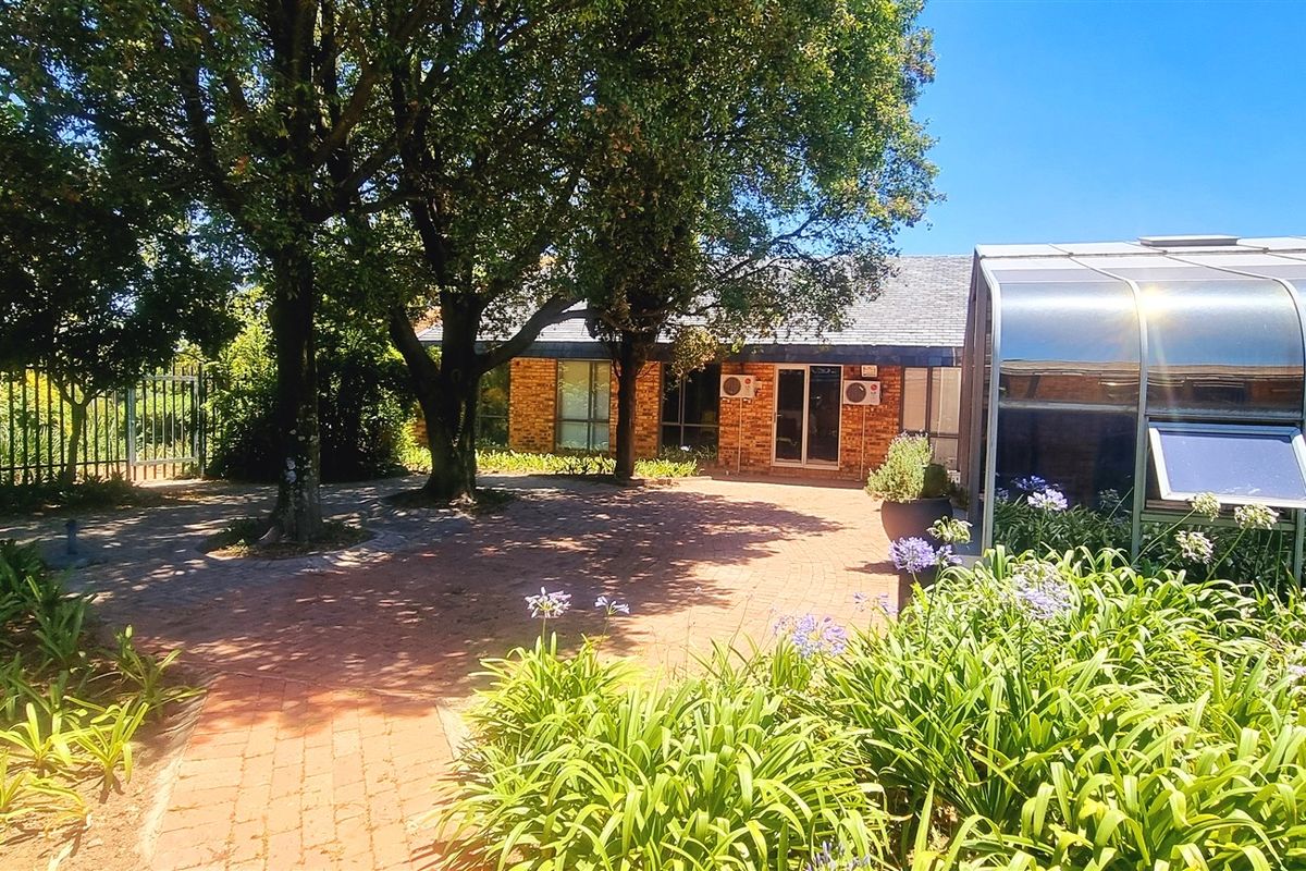 A view of the office exterior featuring a brick-paved courtyard, mature trees, and a covered structure with glass panels.