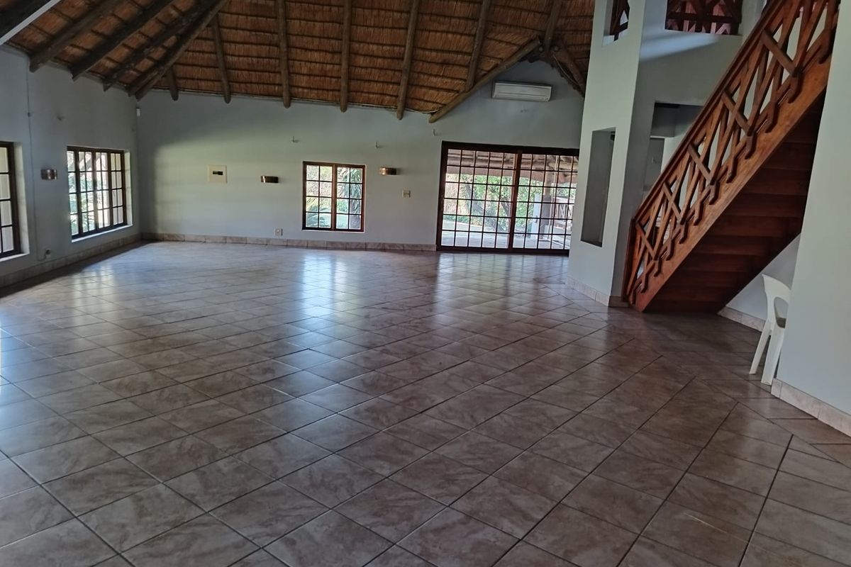 Spacious open-plan living area featuring a high thatched ceiling with exposed rafters, tiled flooring, and a timber staircase leading to an upper level.