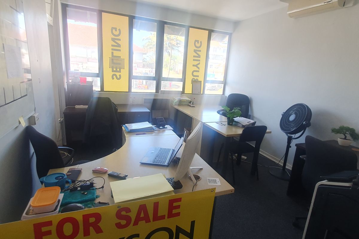 A functional office space featuring large windows for natural light, carpeted flooring, and a wall-mounted air conditioning unit.