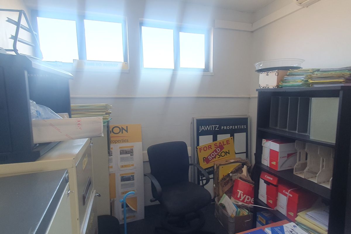 A compact office space featuring high-level sliding windows and an integrated air conditioning unit, currently utilized for storage and administrative tasks.