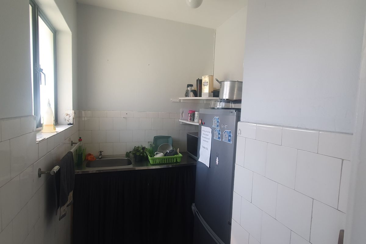 A compact kitchenette area featuring a stainless steel sink, tiled splashback, and open wall shelving, suitable for a small office breakroom.