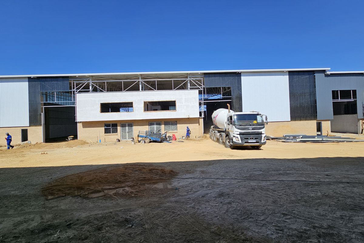 A large industrial warehouse facility currently under construction, featuring steel frame structure, metal cladding, and brick facade elements.