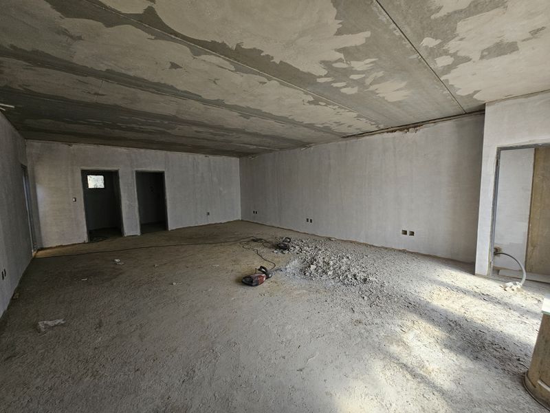 An open-plan industrial space currently under construction, featuring raw concrete ceilings, plastered walls, and unfinished flooring, suitable for custom fit-out.