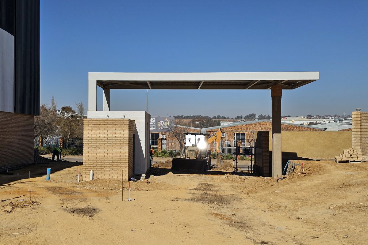 Front entrance area of an industrial property featuring a modern concrete canopy and brick gatehouse structure under construction.