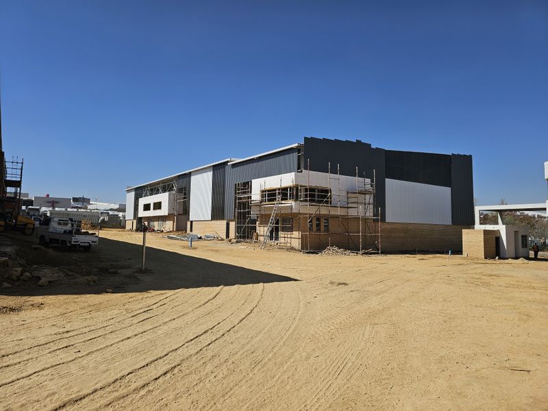 An industrial warehouse property currently under construction, featuring metal cladding, brick facade, and active scaffolding on site.
