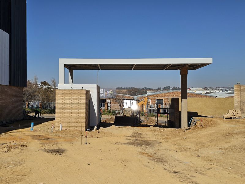 Front entrance area of an industrial property featuring a modern concrete canopy and brick gatehouse structure under construction.