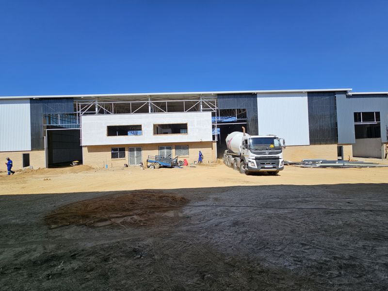 A large industrial warehouse facility currently under construction, featuring steel frame structure, metal cladding, and brick facade elements.