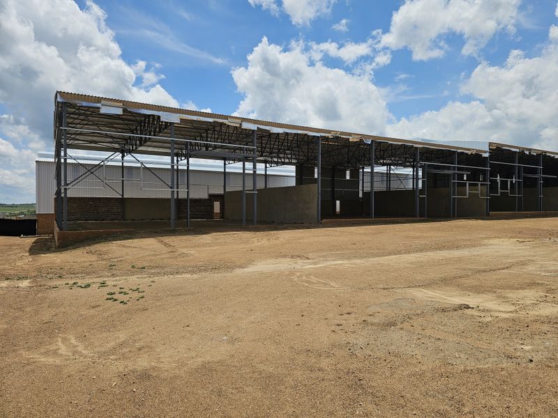 An industrial property under construction featuring a steel portal frame structure with corrugated metal roofing and partial brick masonry walls.