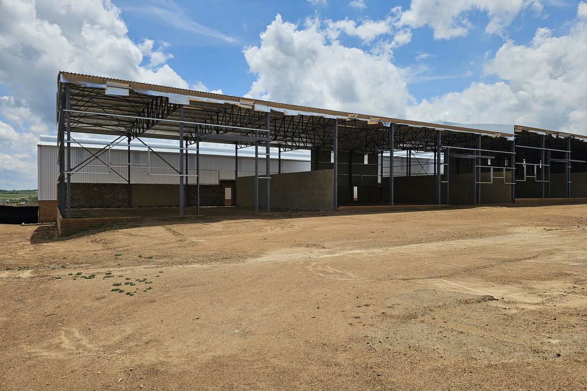 An industrial property under construction featuring a steel portal frame structure with corrugated metal roofing and partial brick masonry walls.