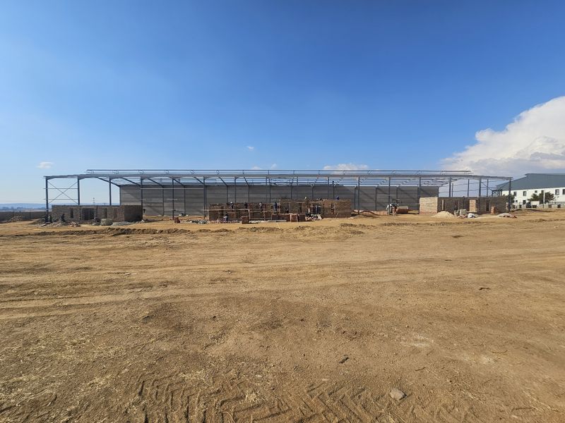 Wide view of an industrial property under construction, featuring a steel portal frame structure and ongoing brick masonry work on a large site.