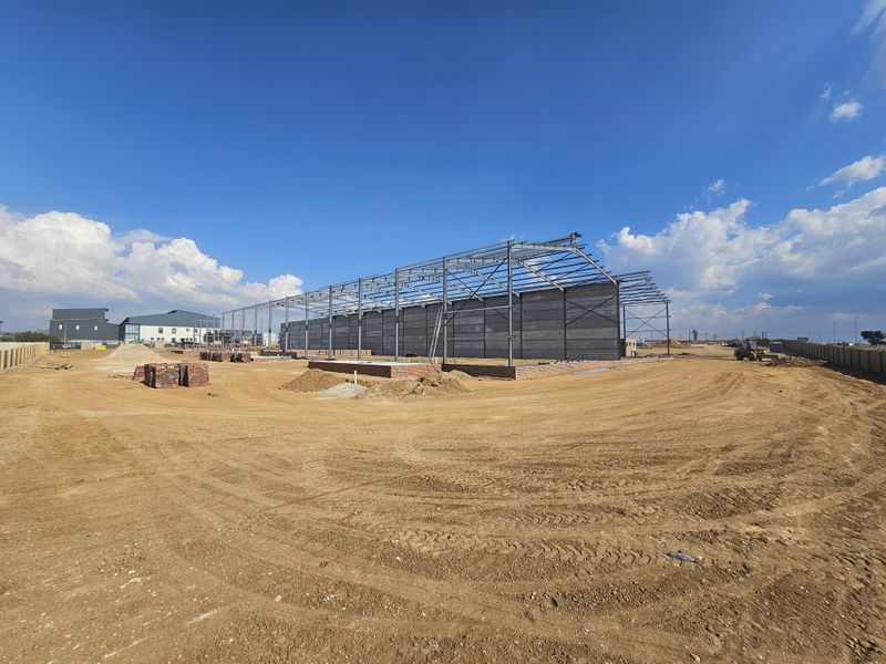 A wide-angle view of an industrial property under construction, featuring a steel portal frame structure and precast concrete wall panels on an unpaved site.