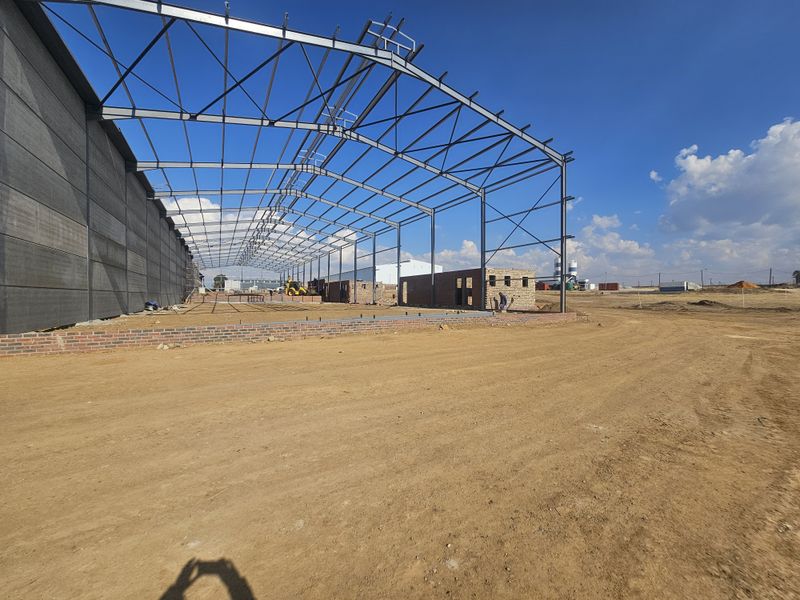 An industrial property under construction featuring a steel portal frame structure and precast concrete wall panels on a large site.