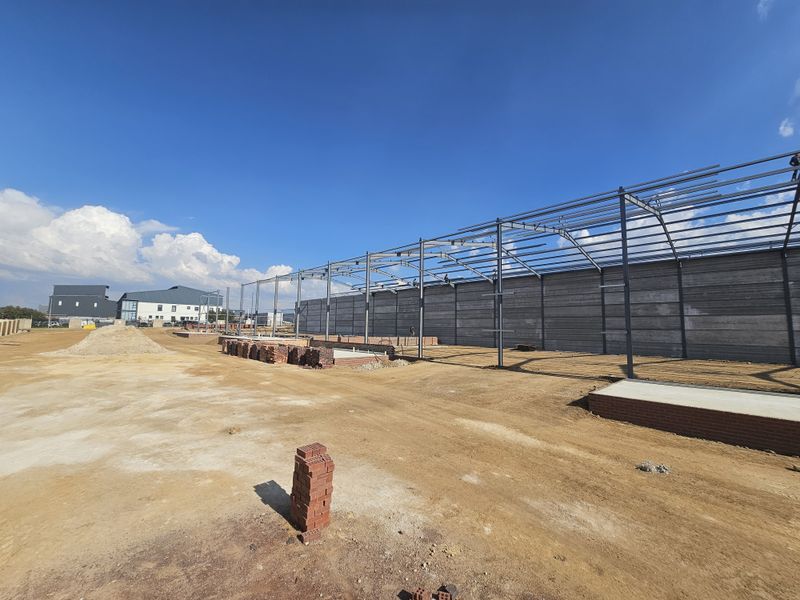 Industrial site under construction featuring a steel portal frame structure and precast concrete wall panels on an unpaved lot.