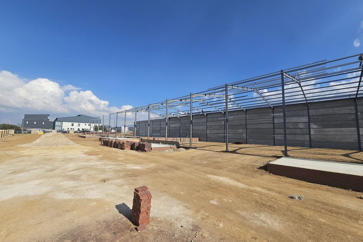 Industrial site under construction featuring a steel portal frame structure and precast concrete wall panels on an unpaved lot.