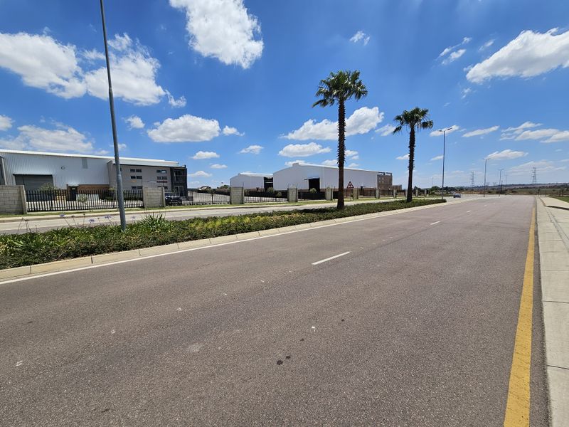 A clear street-level view of the industrial park approach, featuring paved roads, perimeter fencing, and well-maintained landscaping.