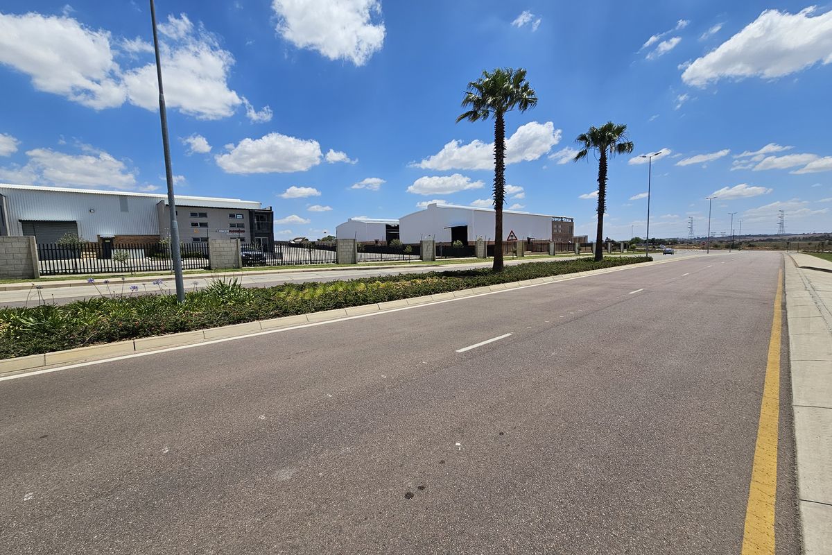 A clear street-level view of the industrial park approach, featuring paved roads, perimeter fencing, and well-maintained landscaping.