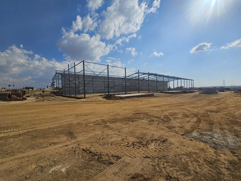 Industrial property under construction featuring a steel portal frame structure and concrete wall panels on a large unpaved site.